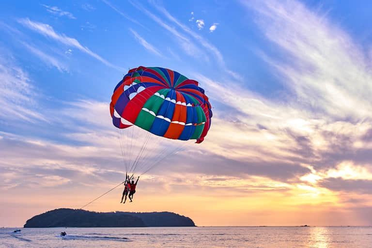 Couple soaring high above a tranquil sunset sea on a colorful parasail